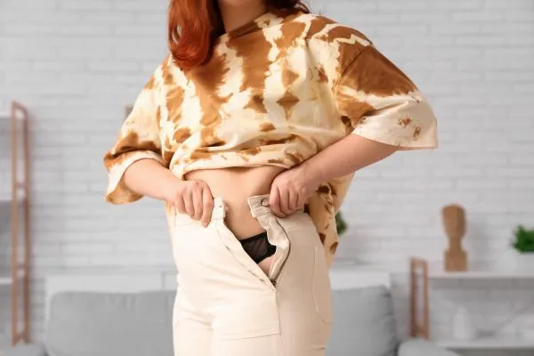 Image of woman trying to do her trousers up after pregnancy weight gain Isleworth