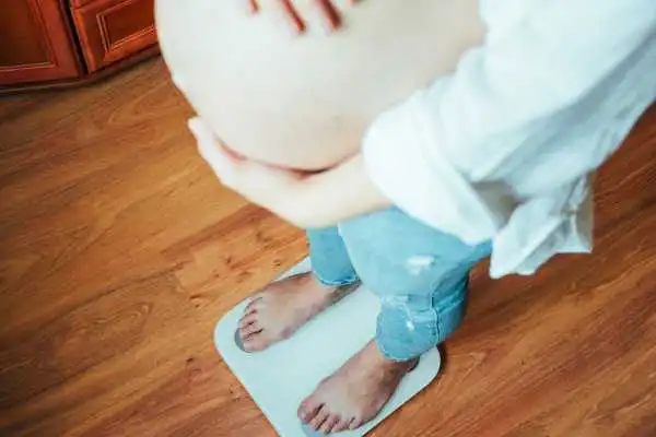 Image of woman weighing herself and experiencing weight gain through pregnancy Isleworth